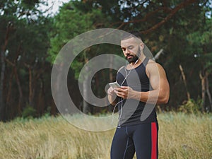 A muscular handsome bodybuilder with a tattoo on his shoulder listening music after a workout on a natural background.