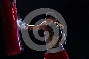 Muscular handsome boxer giving a forceful forward kick during a practise round with a boxing bag.