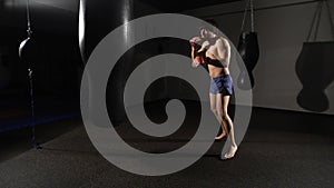 Muscular handsome fighter giving a forceful forward kick during a practise round with a boxing bag.