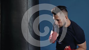 Muscular handsome fighter giving a forceful forward kick during a practise round with a boxing bag, kickboxing. Close up