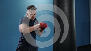 Muscular handsome fighter giving a forceful forward kick during a practise round with a boxing bag, kickboxing. Close up