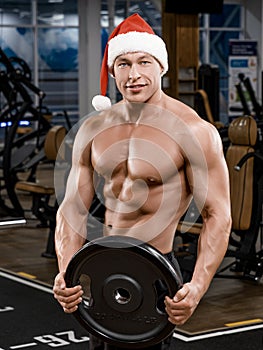 Muscular handsome sexy bodybuilder Santa Claus holding weight in the hands