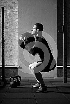 Muscular hard working man squatting with a med ball