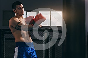 Muscular hardworking fighter practicing with punching bag indoor.