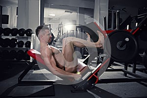 Muscular legs, handsome bodybuilder workout on trainer in the gym