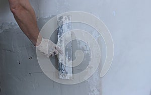 Muscular male arm with a wide spatula against a wall background