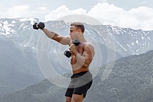 Muscular male athlete with arms raised doing lifting exercises dumbbells.