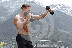 Muscular male athlete with arms raised doing lifting exercises dumbbells.