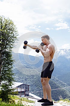 Muscular male athlete with arms raised doing lifting exercises dumbbells.