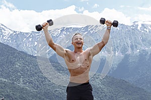 Muscular male athlete with arms raised doing lifting exercises dumbbells.