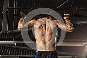 Muscular male athlete doing pull-ups on horizontal bar at the gym