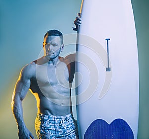 Muscular male body on blue background. Sexy surfer surfing man with surfboard.