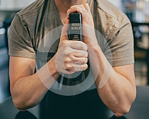 muscular male fitness model holds bible tightly in hands with Holy Bible visible