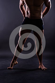 Muscular male legs, man in studio, dark background