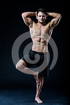 Muscular man balancing on the one leg feeling relaxed dark background