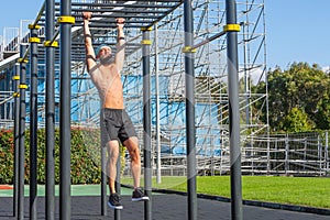 Muscular man in a bandana hanging on the stairs intercepted on the rungs with his hands in the park outdoors