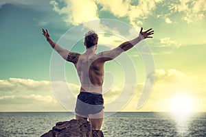 Muscular man on the beach in front of rising sun