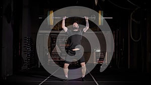 Muscular Man with Beard Does Overhead Deadlift with Barbell on Dark Background