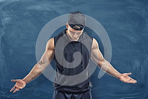 Muscular man in black clothes and cap with his head lowered on blue chalkboard background.