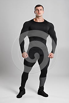 Muscular man in black compression sportswear on gray background