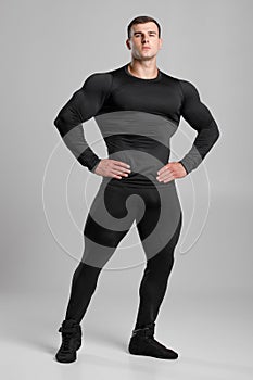 Muscular man in black compression sportswear on gray background