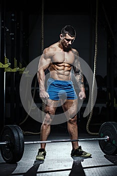 Muscular man bodybuilder prepares for lifting heavy barbell in gym. Fit muscle guy workout with weights and barbell