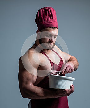 Muscular man cook in chef apron hold plate and beater, preparing food