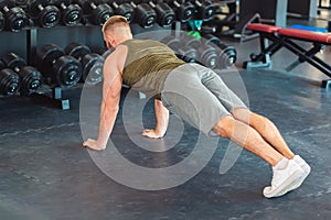 A muscular man does push-ups on the gym floor. Top view, from the back. Sports and warm-up