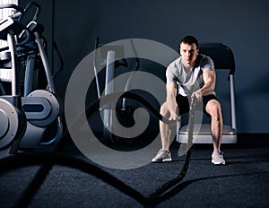 Muscular Man is Doing Battle Rope Exercise in Modern Fitness Gym. CrossFit and Healthy Lifestyle Concept. photo