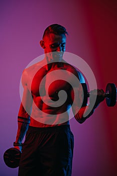 A muscular man is doing bicep curls with dumbbells under blue and red lights