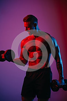 A muscular man is doing bicep curls with dumbbells under blue and red lights