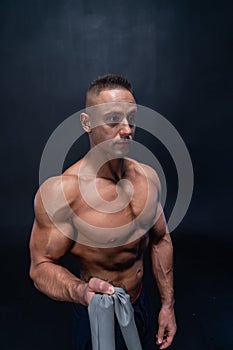 Muscular man doing calisthenic exercise with power band isolated on the black background