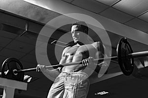 Muscular man doing crossfit. Fit man doing biceps lifting barbell. Young man working out at crossfit gym. Athletic guy