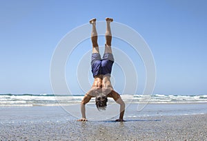 Muscular man doing handstand on beach photo