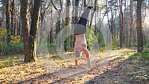 Muscular man doing handstand in forest at beautiful sunset background. Strong gymnast training at scenic environment