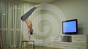 A muscular man doing handstand and watch TV. Concept of originality, creativity and outstanding