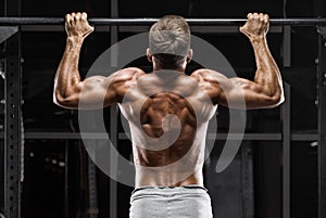 Muscular man doing pull up on horizontal bar in gym, working out. Strong fitness male showing back photo