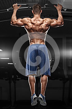 Muscular man doing pull up on horizontal bar in gym, working out. Strong fitness male pulling up, showing back