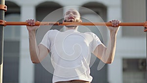 Muscular man doing pull-ups on horizontal bar. on workout area near house