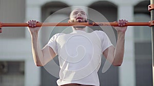 Muscular man doing pull-ups on horizontal bar. on workout area near house