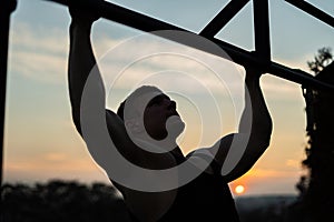 Muscular man doing pullups on sunset sky background. Calisthenics, healthy lifestyle and workout concept