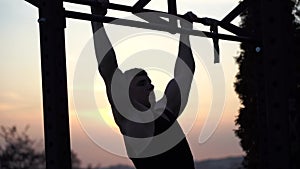 Muscular man doing pullups on sunset sky background. Concept of willpower, motivation and passion