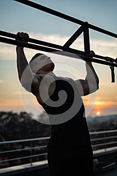 Muscular man doing pullups on sunset sky background. Concept of willpower, motivation and passion