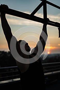 Muscular man doing pullups on sunset sky background. Concept of willpower, motivation and passion