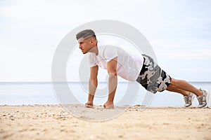 Muscular man doing push up on beach. Body training