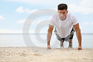 Muscular man doing push up on beach, space for text. Body training
