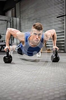 Muscular man doing push up with kettlebells