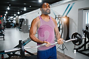 Muscular man doing weight lifting exercise at gym with copy space. Side view of fit african american guy standing with