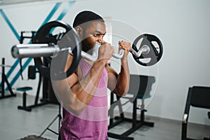 Muscular man doing weight lifting exercise at gym with copy space. Side view of fit african american guy standing with