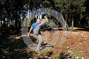 Muscular man doing workout is warming up by rising leg up in the air exercise in forest.